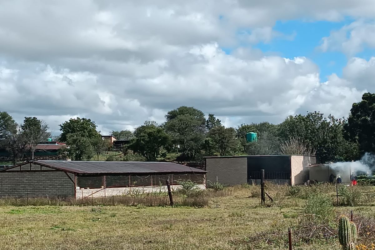 View of the small holding property featuring multiple outbuildings, brick structures, and a water storage tank set within a rural landscape.