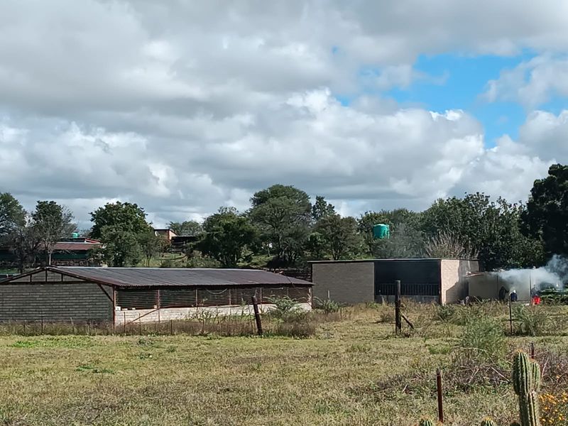 View of the small holding property featuring multiple outbuildings, brick structures, and a water storage tank set within a rural landscape.