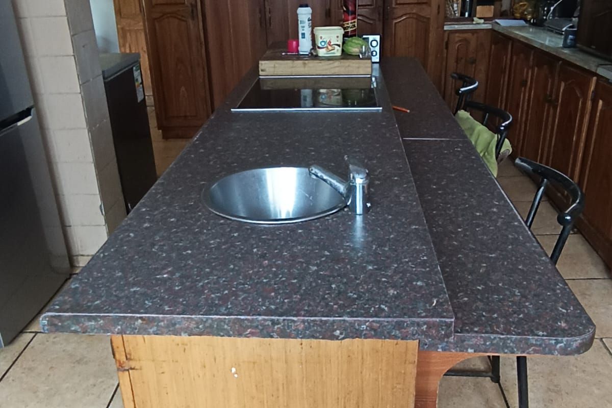 A functional kitchen featuring a central island with a prep sink and integrated hob, surrounded by traditional wooden cabinetry and tiled flooring.