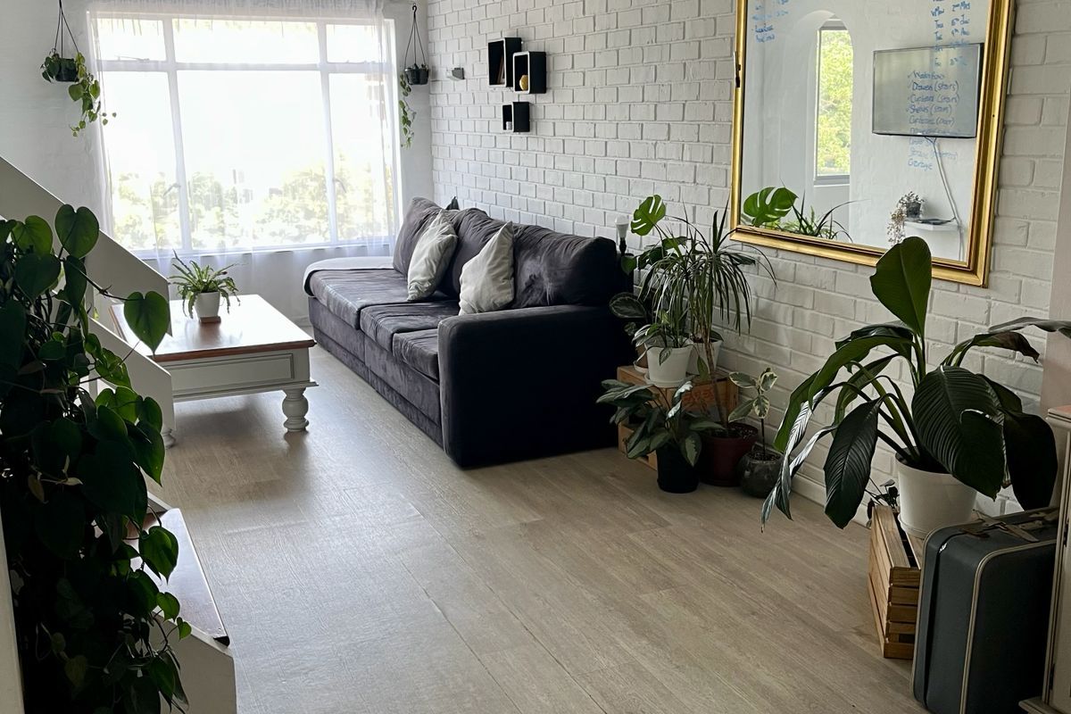 Bright living room featuring a vaulted timber ceiling, painted brick feature wall, and modern laminate flooring with ample natural light.