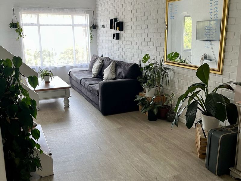 Bright living room featuring a vaulted timber ceiling, painted brick feature wall, and modern laminate flooring with ample natural light.