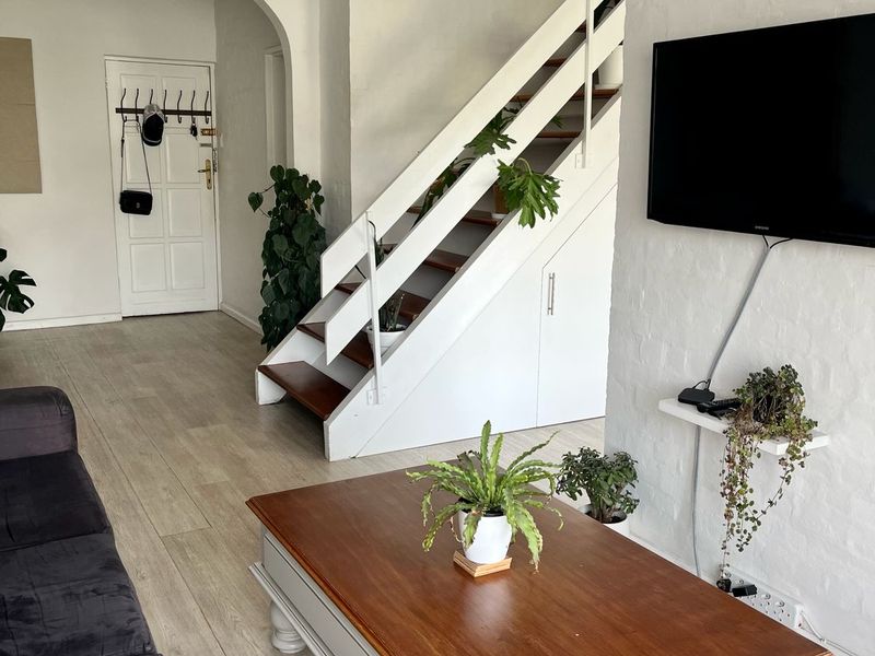 A bright living room featuring a staircase with integrated under-stair storage, white painted brick walls, and light-toned laminate flooring.