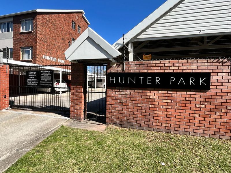 Front entrance view of Hunter Park apartment complex featuring a brick boundary wall, secure metal gates, and electric fencing.