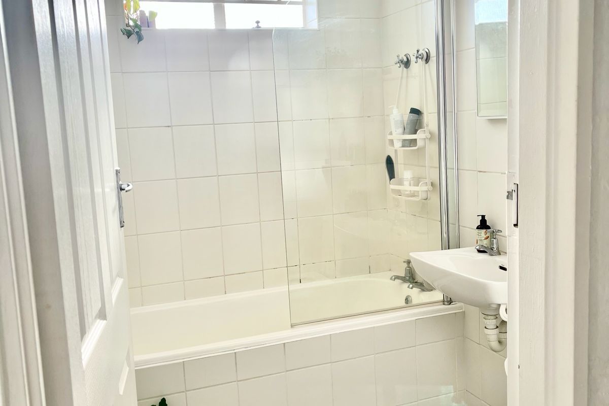 A functional bathroom featuring a combined bathtub and shower, pedestal basin, toilet, and neutral tiled finishes throughout.