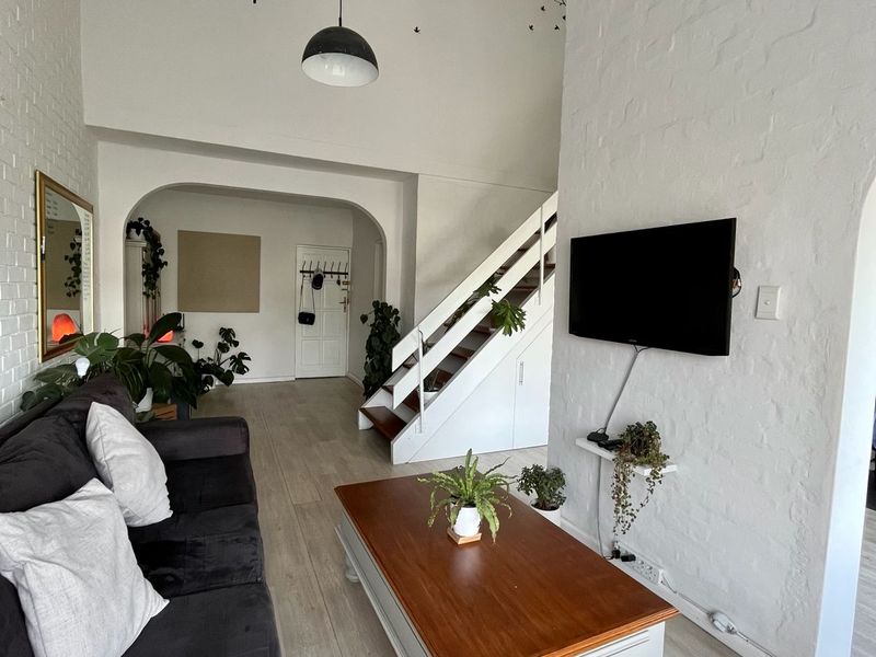 A bright living room featuring high ceilings, painted brick walls, a staircase, and laminate flooring, creating an open and airy atmosphere.