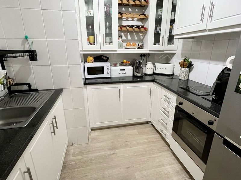 A well-maintained kitchen featuring white cabinetry, dark granite countertops, integrated oven, electric cooktop, and light wood-look flooring.