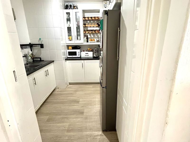 A functional galley-style kitchen featuring white cabinetry, black countertops, tiled splashbacks, and wood-look flooring, offering a clean and practical workspace.