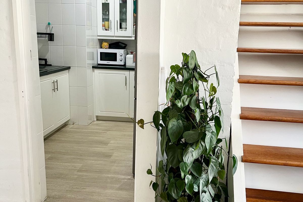 A view into a functional kitchen with white cabinetry and tiled backsplash, adjacent to a timber staircase in an open-plan apartment setting.