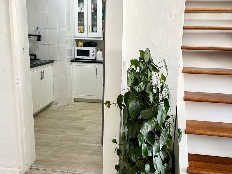 A view into a functional kitchen with white cabinetry and tiled backsplash, adjacent to a timber staircase in an open-plan apartment setting.