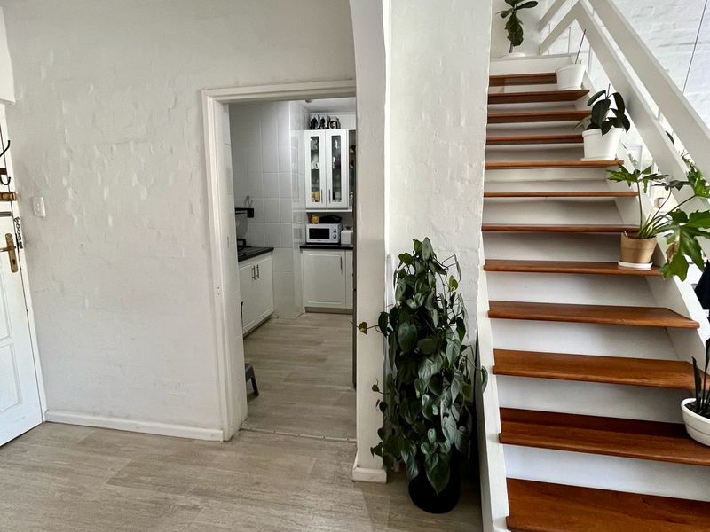 A bright hallway featuring a wooden staircase with white balustrades, laminate flooring, and an arched entryway leading into the kitchen area.