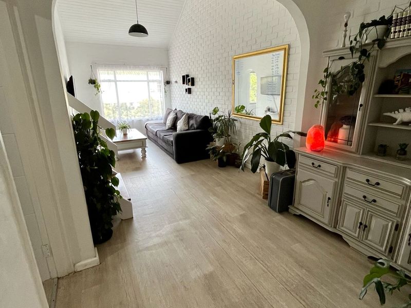 A bright living room featuring a vaulted ceiling, exposed white brick wall, and light-toned laminate flooring, accessed through a characterful arched doorway.