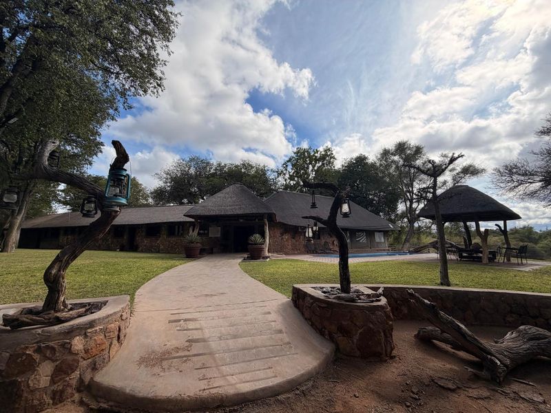 Rear view of a farm-style property featuring a thatched roof, stone exterior, swimming pool, and a landscaped garden with a stone-paved entrance path.