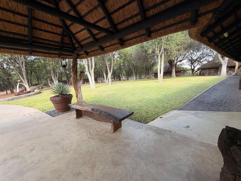 A covered patio area with a traditional thatched roof and exposed timber beams, overlooking a spacious, well-maintained garden on the farm property.
