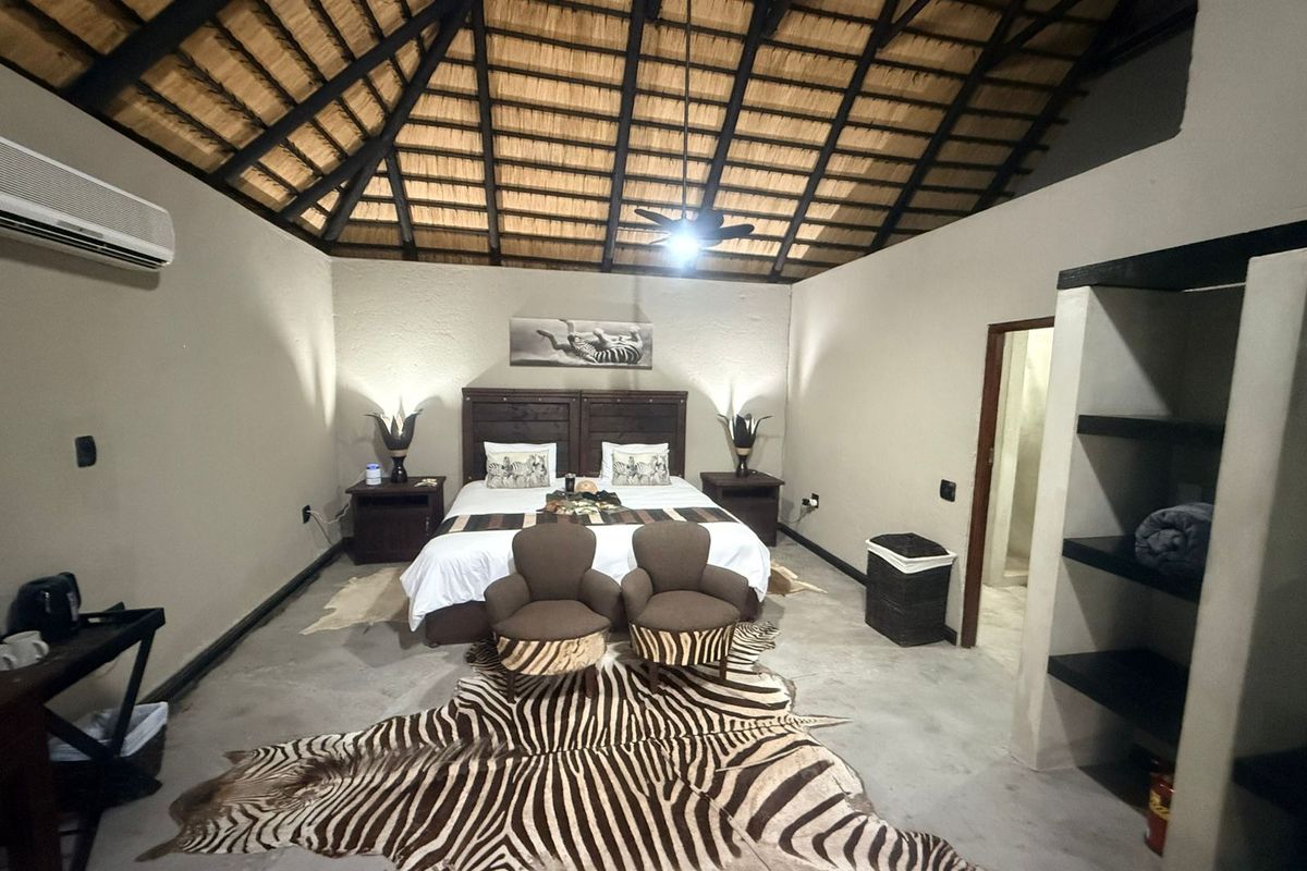 Spacious bedroom featuring a high thatched roof with exposed timber rafters, polished concrete floors, air conditioning, and built-in shelving.