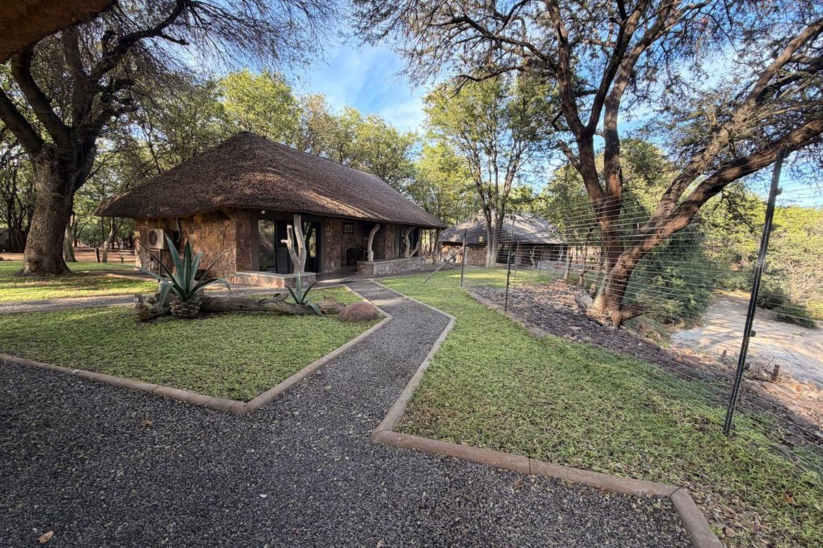 A well-maintained farm cottage featuring traditional thatch roofing and natural stone cladding, surrounded by landscaped grounds and gravel pathways.