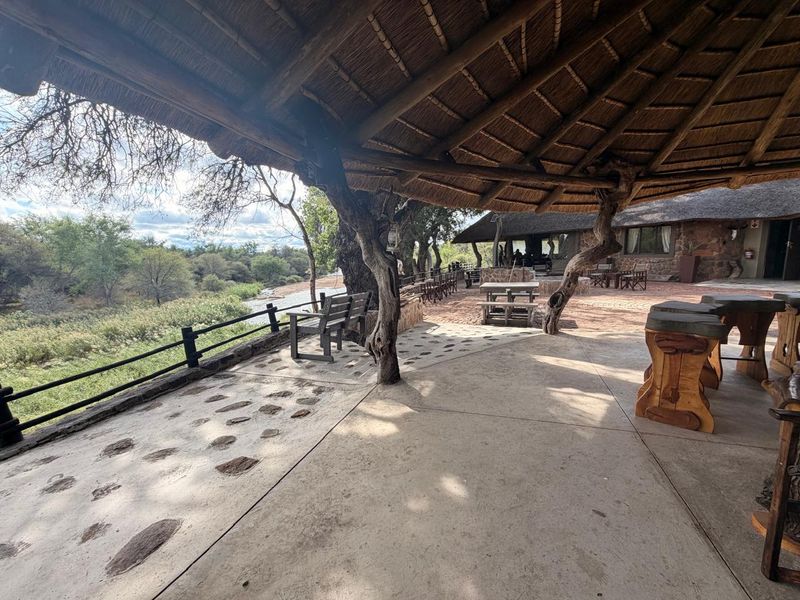 Spacious covered patio featuring a traditional thatched roof, stone flooring, and scenic views of the surrounding natural landscape.