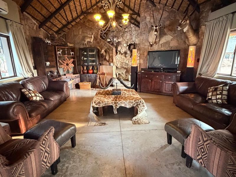 Spacious living room featuring a high vaulted thatched ceiling with exposed timber trusses, stone feature wall, and polished concrete flooring.