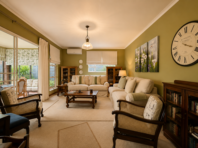 A well-maintained living room featuring neutral carpeting, olive-toned walls, and large sliding glass doors that provide seamless access to the outdoor patio area.