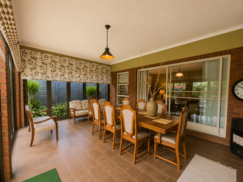 A spacious covered patio featuring tiled flooring, exposed brick walls, and large sliding glass doors that provide seamless access to the garden area.