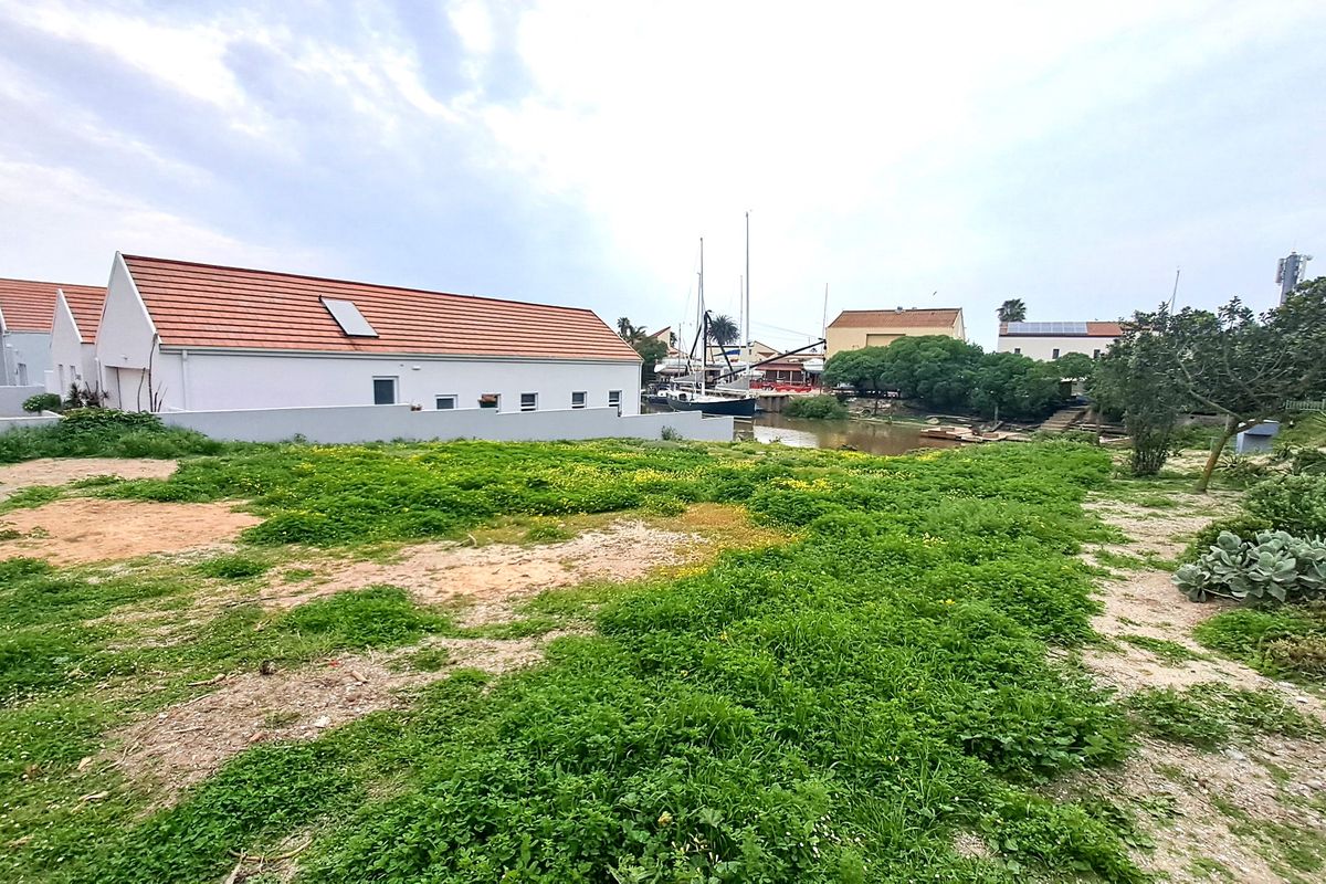A view of a vacant residential plot featuring natural vegetation, adjacent to a residential building with a tiled roof and boundary wall.