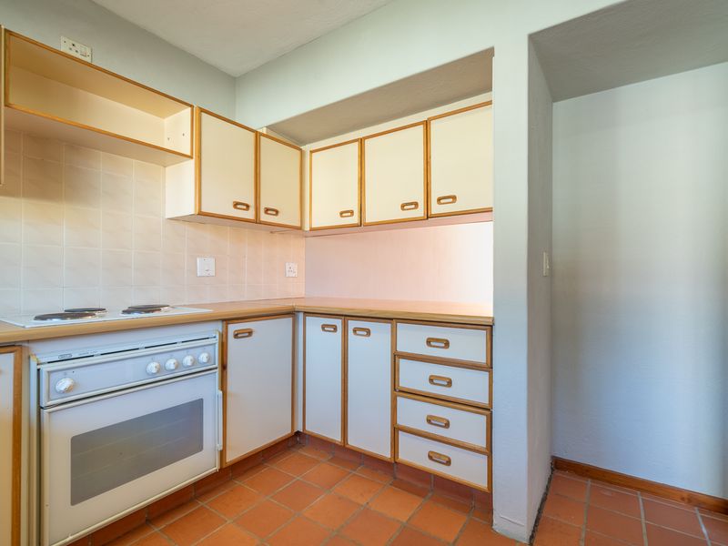 A functional kitchen featuring dated cabinetry, laminate countertops, a built-in oven with electric hob, and traditional terracotta floor tiles.