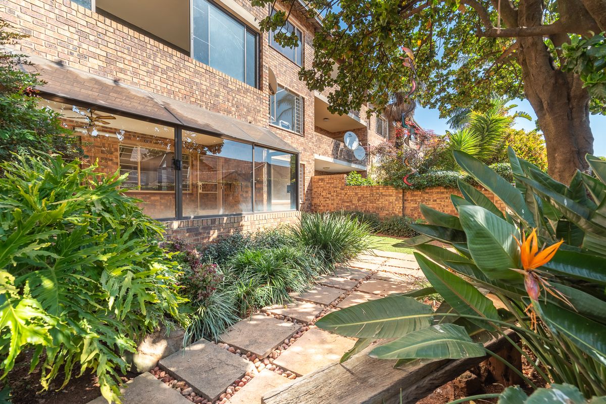 Rear view of the apartment building featuring a face brick facade, an enclosed patio area, and a landscaped garden with a paved walkway.