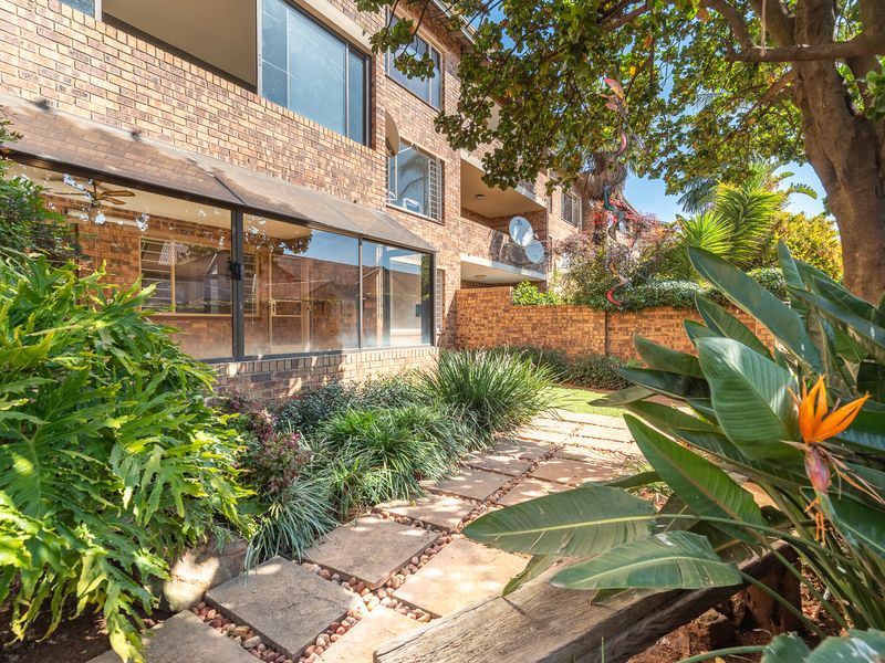 Rear view of the apartment building featuring a face brick facade, an enclosed patio area, and a landscaped garden with a paved walkway.