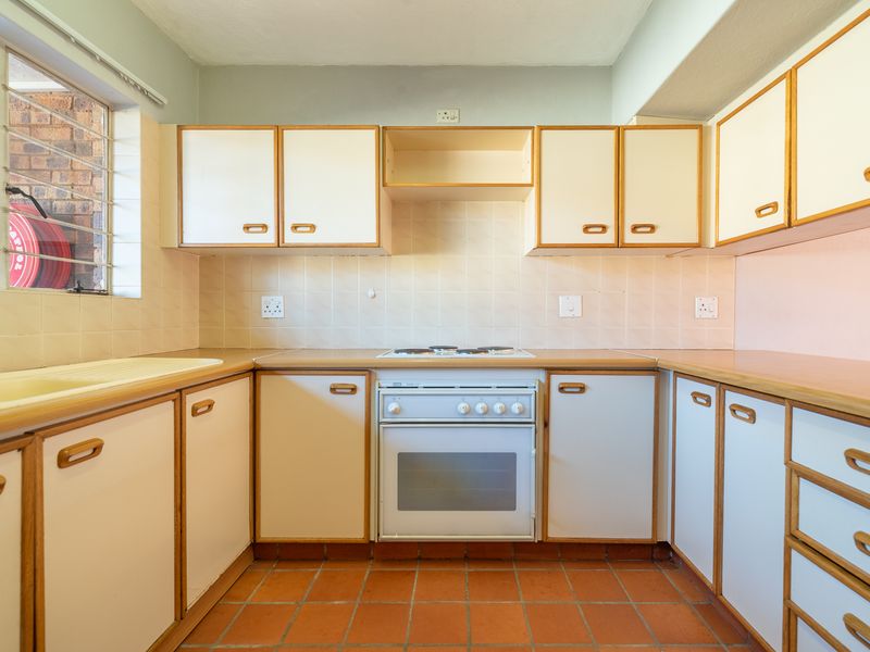 A functional kitchen featuring built-in cabinetry, laminate countertops, an integrated oven and stove, and classic terracotta floor tiles.