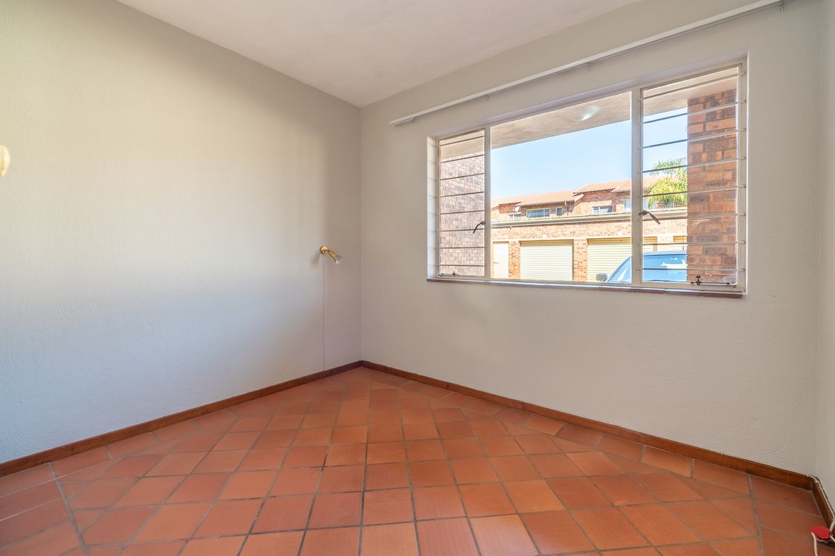 A bright, empty bedroom featuring traditional terracotta floor tiles and a large window with security bars, offering a blank canvas for personalization.