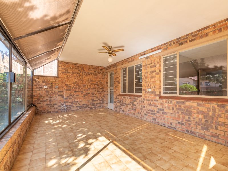 A spacious, enclosed patio featuring exposed brick walls, tiled flooring, and a ceiling fan, offering a versatile outdoor living space.