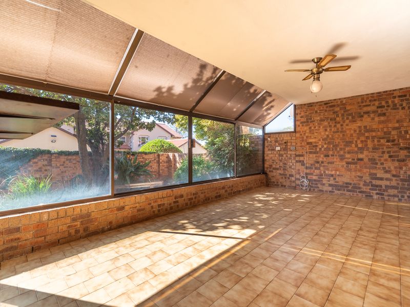 A spacious, enclosed patio featuring exposed brick walls, tiled flooring, and large windows that provide ample natural light and garden views.