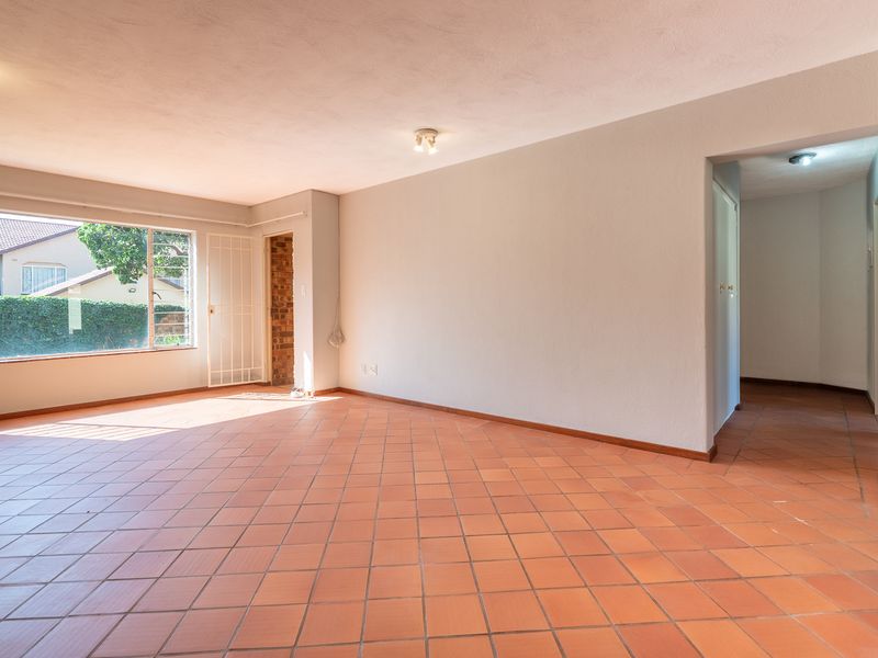 Spacious, sunlit living area featuring terracotta tile flooring, large windows, and neutral wall finishes, offering a versatile blank canvas for interior design.