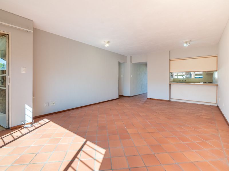 Spacious open-plan living area featuring terracotta floor tiles, a kitchen pass-through window, and direct access to an outdoor patio area.