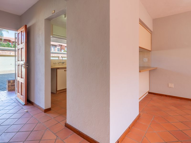 An empty kitchen area featuring terracotta floor tiles, built-in cabinetry, and laminate countertops, with direct access to an exterior paved area.