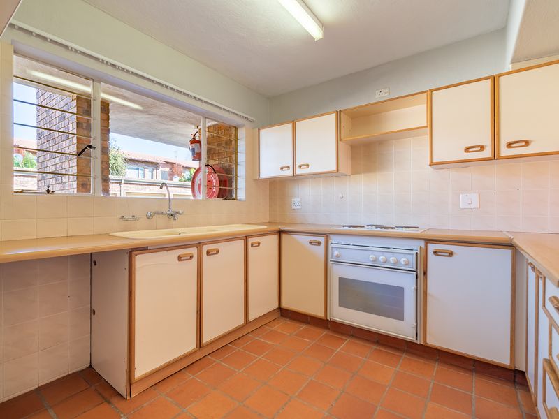 A functional kitchen featuring built-in cabinetry, laminate countertops, a built-in oven with hob, and terracotta floor tiles, offering potential for modernization.