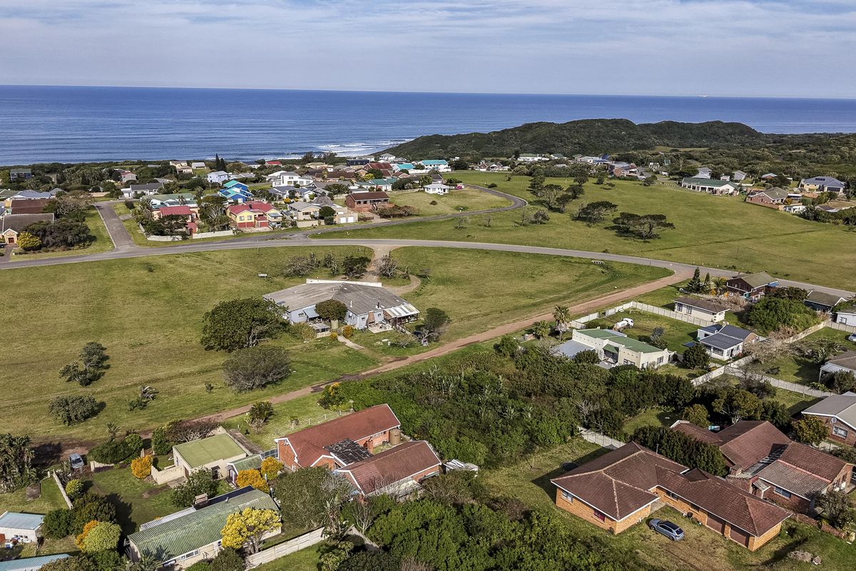 An aerial view of a coastal residential neighborhood featuring open grassland, established homes, and proximity to the ocean.