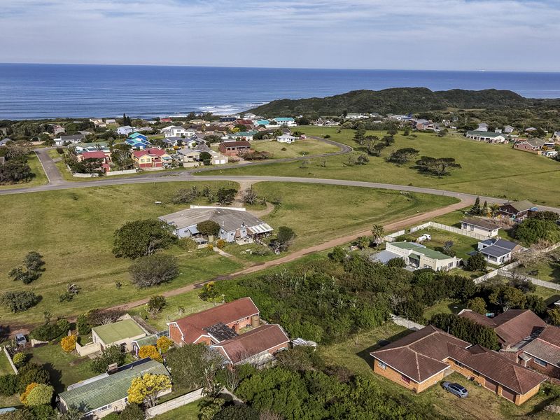 An aerial view of a coastal residential neighborhood featuring open grassland, established homes, and proximity to the ocean.