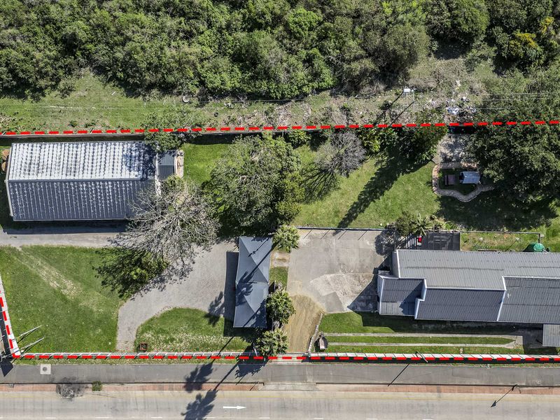 Aerial view of the property showing the main dwelling, outbuildings, paved driveway, and surrounding garden area within the marked boundary.