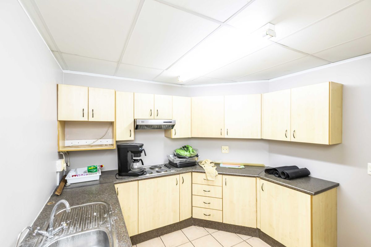 A functional kitchen featuring light wood-finish cabinetry, laminate countertops, a stainless steel sink, and an integrated electric hob with an extractor fan.