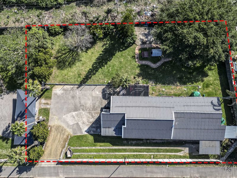 Aerial view of the property showing the house with a corrugated metal roof, concrete driveway, and a spacious garden area.