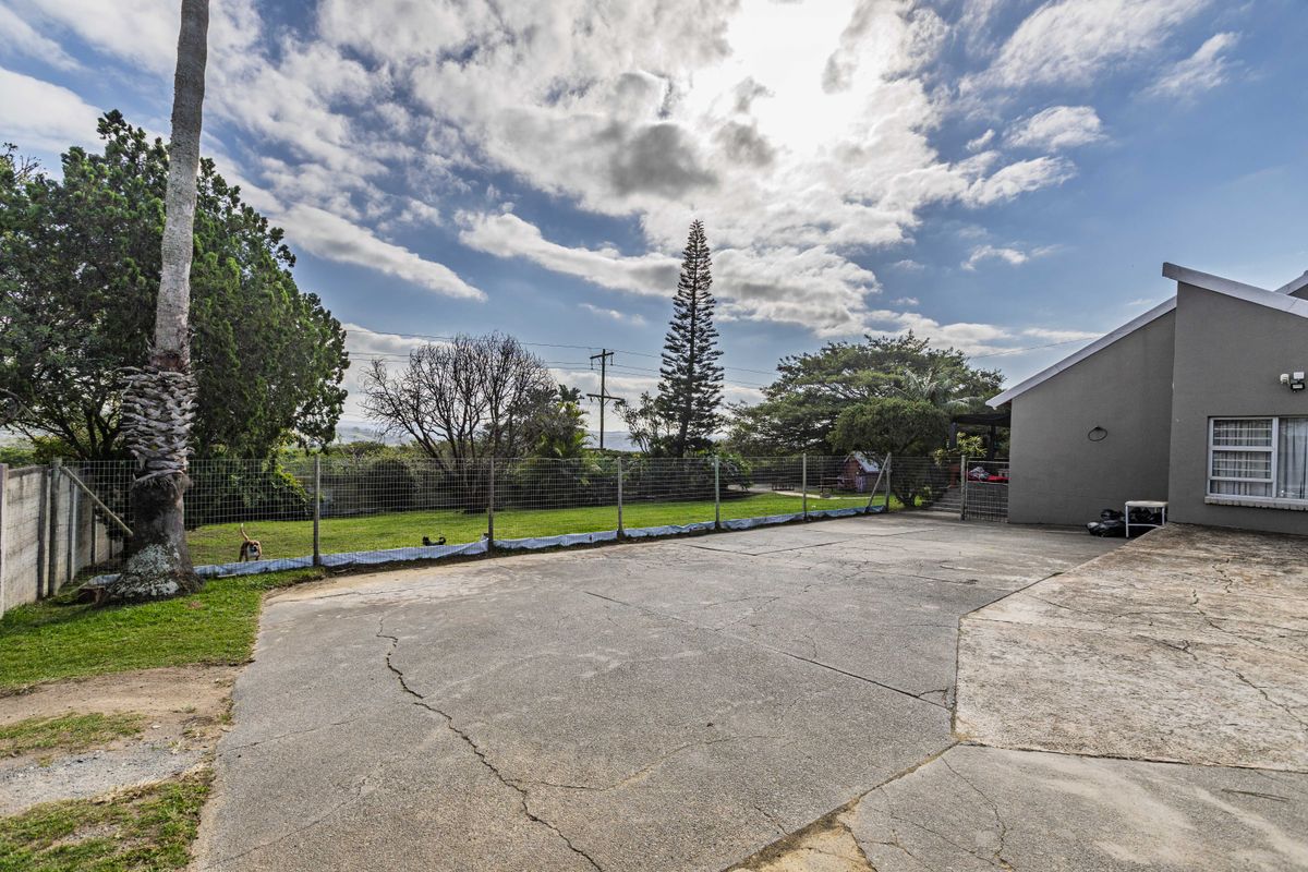 A spacious rear exterior area featuring a large concrete driveway with visible cracking, enclosed by wire mesh fencing and a grass lawn.