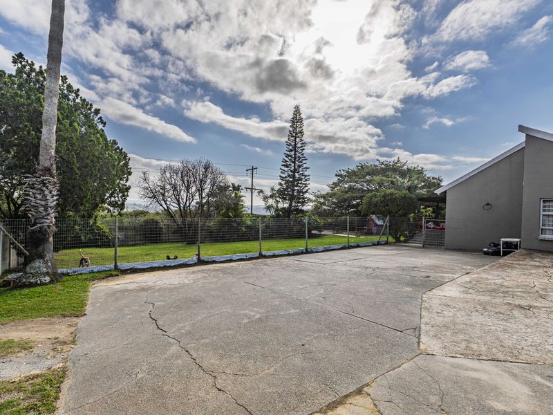 A spacious rear exterior area featuring a large concrete driveway with visible cracking, enclosed by wire mesh fencing and a grass lawn.