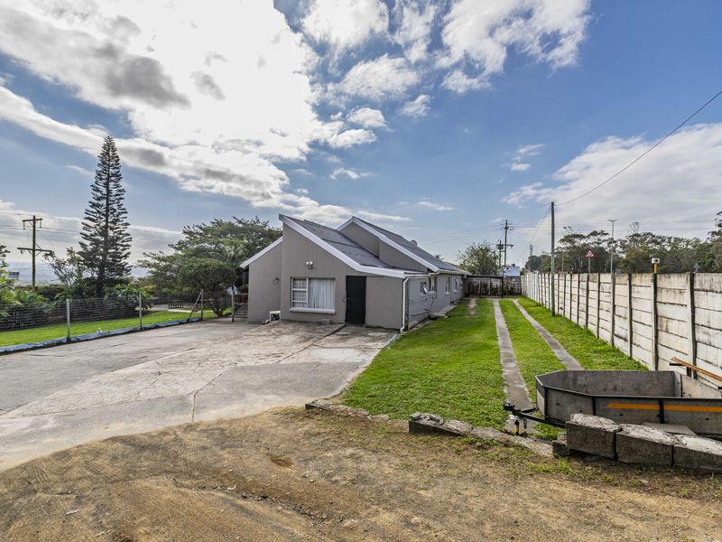 Front exterior view of a single-story house featuring a concrete driveway, metal roofing, and a precast concrete boundary wall.