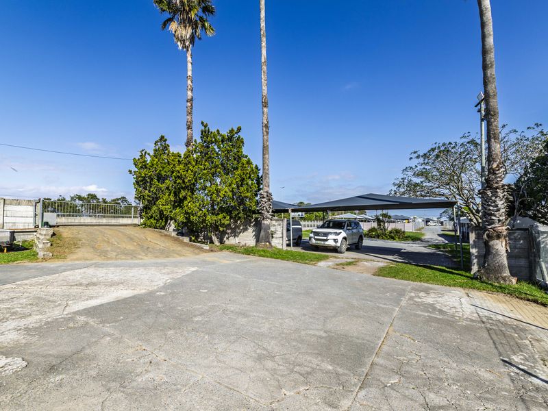Front exterior view featuring a concrete driveway, perimeter wall, sliding gate, and a covered carport area.