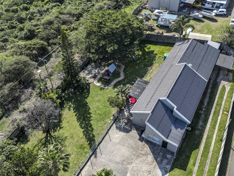 Aerial view of the property showing the main dwelling with a corrugated metal roof, concrete driveway, and spacious garden area.