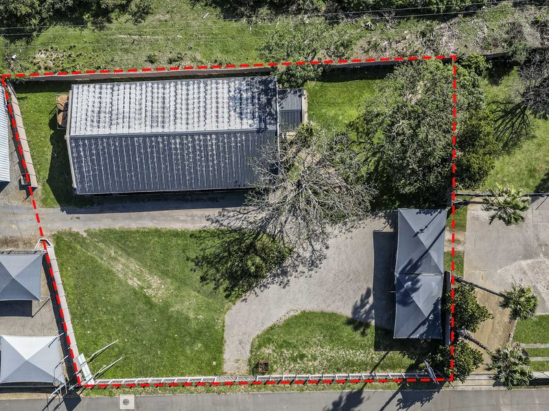 Aerial view of the property showing the main building with a corrugated metal roof, gravel driveway, lawn area, and perimeter fencing.