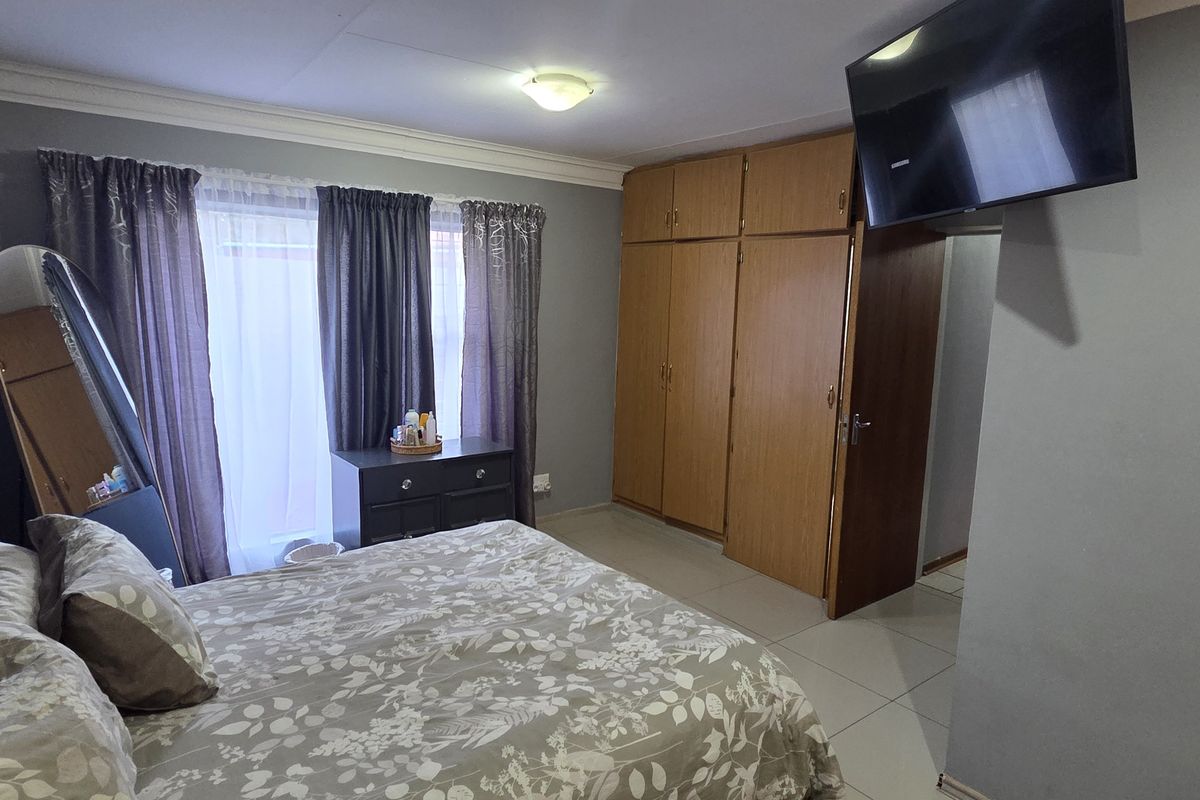 A functional bedroom featuring built-in wooden cupboards, tiled flooring, and an installed air conditioning unit.