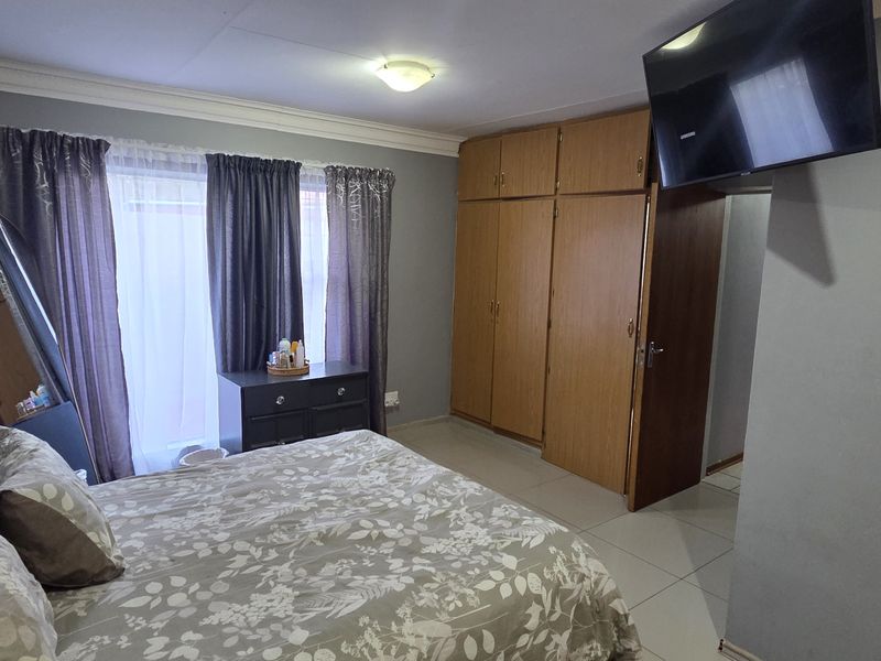 A functional bedroom featuring built-in wooden cupboards, tiled flooring, and an installed air conditioning unit.