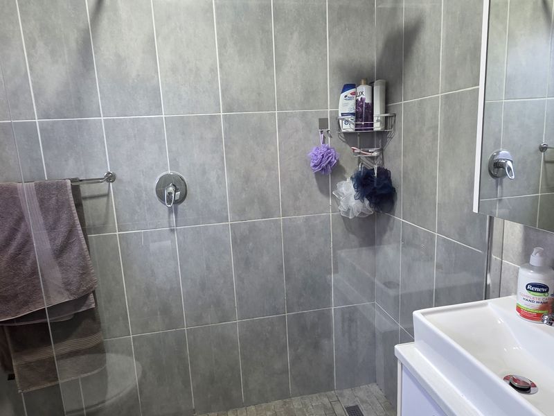 A modern bathroom featuring a glass-enclosed shower with grey wall tiles, a vanity basin with chrome fixtures, and a wall-mounted mirror.