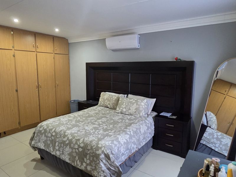 A well-maintained bedroom featuring built-in wooden cupboards, tiled flooring, recessed lighting, and a wall-mounted air conditioning unit.